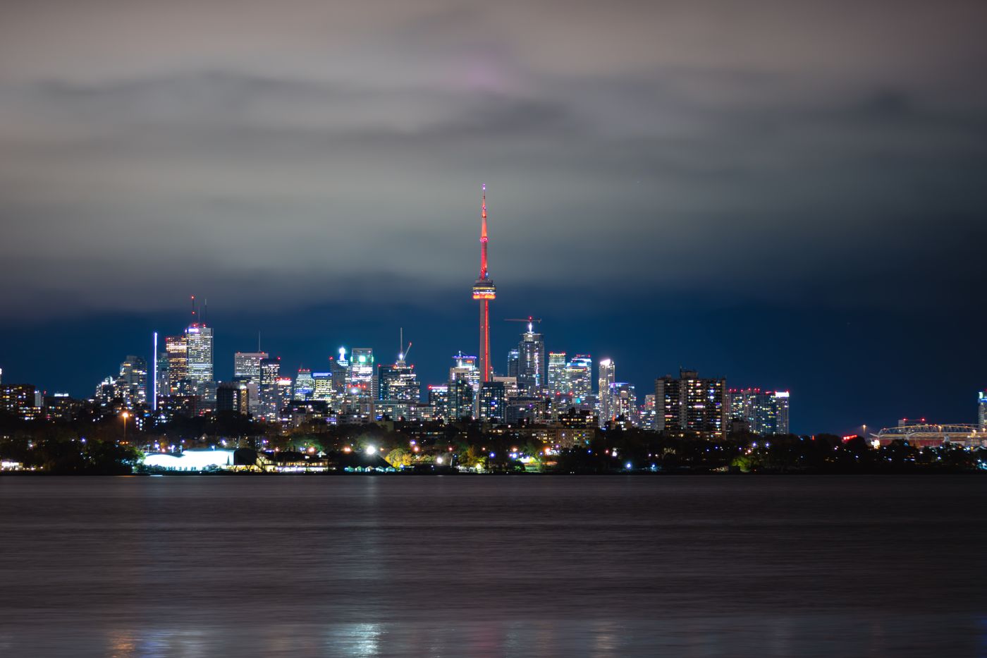 The Toronto skyline and CN Tower lit up at night, reflected on the lake.