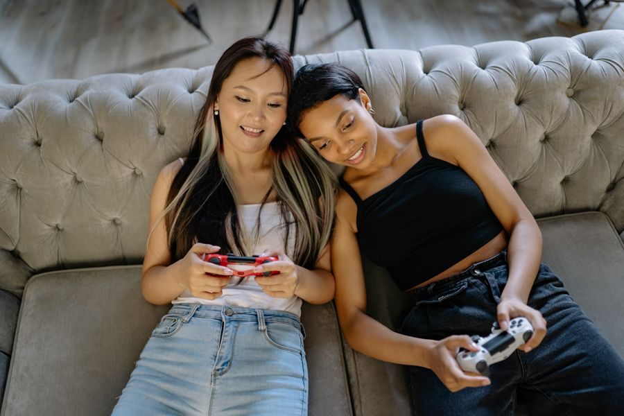 Two adults laughing on a sofa while playing a video game together.